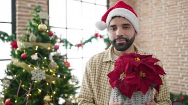 Noel Baba şapkalı gülümseyen bir adam. Çiçekler evde. Noel kutlaması için süslenmiş.