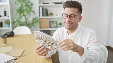 Neşeli genç İspanyol erkek çalışan başarıyı kutluyor, dolar saçıyor ve ofise para harcıyor.