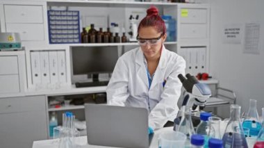 Ciddi genç İrlandalı bilim adamı, laboratuvarda çalışan kızıl saçlı güzel bir kadın, elinde deney tüpü, ve dizüstü bilgisayar veri analizi üzerinde yoğunlaşıyor.