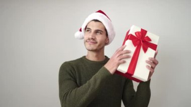 Gri arka planda hediye kutusu olan Noel Baba şapkalı mutlu bir genç.