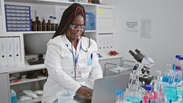 興奮したアフリカ系アメリカ人女性科学者 彼女のブレード メガネをロックし ラップトップ上の医学の驚異を模索しながらラボで勝利祝いのジェスチャーを打つ — ストック動画