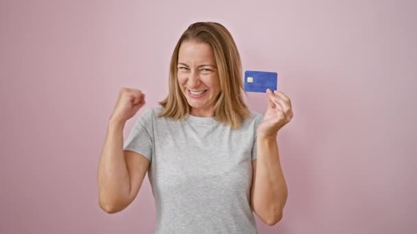 快乐的金发女郎 带着信用卡 带着淡淡的粉红背景 自信地庆祝着 表达着积极和经济上的快乐 — 图库视频影像