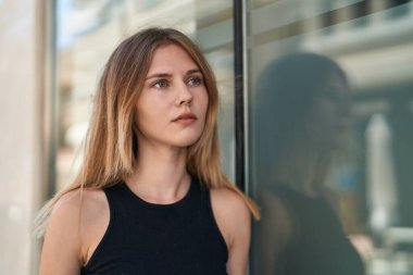 Sokakta ciddi bir ifadeyle yan tarafa bakan genç sarışın kadın.