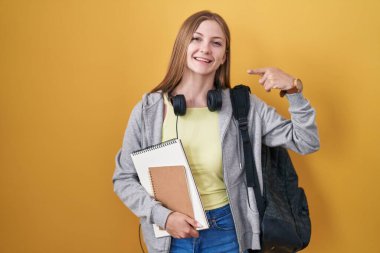 Sırt çantası takan, elinde kitaplarla gülümseyen, parmaklarıyla ve ağzıyla gülümseyen beyaz bir kadın. diş sağlığı kavramı. 