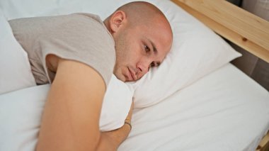 Yatak odasında ciddi bir ifadeyle yatan Latin asıllı genç bir adam.