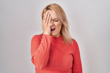Sarışın kadın izole edilmiş arka planda duruyor. Yarı yüzünü, göz ve ağzını eliyle kapatmaktan yoruluyor. Yüzüm acıyor.. 
