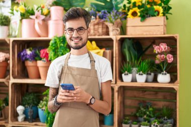 Çiçekçide akıllı telefon kullanarak gülümseyen İspanyol çiçekçi.