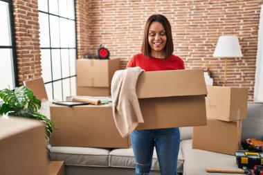 Genç, güzel, İspanyol bir kadın gülümsüyor. Kendine güveni tam. Yeni evinde kıyafetlerle paketi tutuyor.