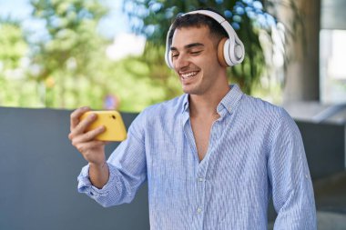 Genç İspanyol adam gülümsüyor. Sokakta akıllı telefondan videolar izliyor.