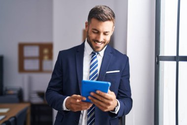 Young hispanic man business worker smiling confident using touchpad at office
