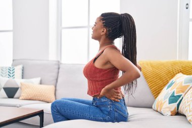 Afrikalı Amerikalı kadın evdeki kanepede oturup sırt ağrısı çekiyor.