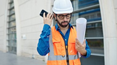 Genç İspanyol mimar elinde planlarla inşaat alanındaki akıllı telefondan gelen sesli mesajı dinliyor.