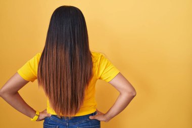 Sarı arka planda duran genç Arap kadın geriye doğru bakıyor kolları vücudunda. 