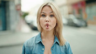 Genç sarışın kadın gülümsüyor. Kendine güveniyor. Komik hareketler yapıyor.