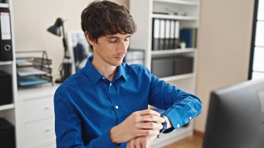 Genç İspanyol iş adamı bilgisayar kullanıyor. Ofiste ciddi yüzlü bir saat kullanıyor.