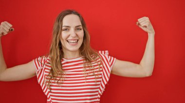 Genç sarışın kadın gülümsüyor kendine güveniyor güçlü hareketler yapıyor kolları izole edilmiş kırmızı arka planda