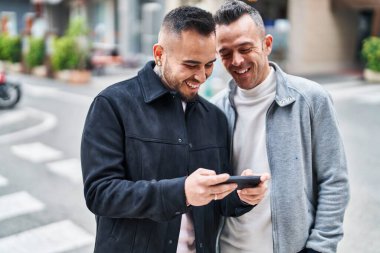 Two men couple smiling confident using smartphone at street