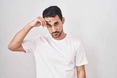 Beyaz arka planda duran yakışıklı İspanyol adam alnındaki sivilceden memnun olmadığını gösteriyor, siyah noktalı çirkin bir enfeksiyon. sivilce ve deri problemi 