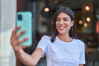 Genç ve güzel İspanyol kadın gülümsüyor. Kendine güveni tam. Sokakta akıllı telefonun yanında selfie çekiyor.