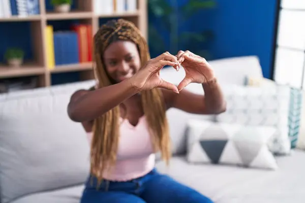 African american woman doing heart gesture with hands sitting on sofa at home