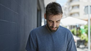 Yakışıklı bir İspanyol genç adam, sakin ama ciddi bir yüz ifadesi ile, şehir caddesinde aşağı bakan serin, güneşli gün ışığında dışarıda duran bir adam