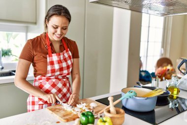 Genç ve güzel İspanyol kadın mutfakta spagetti pişiriyor soğan doğruyor.