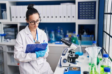 Young caucasian woman scientist weighing pills writing on document at laboratory