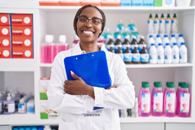 Afro-Amerikalı kadın eczacı gülümseyerek eczanede kendine güvenen bir pano tutuyor.