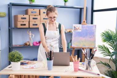 Young caucasian woman artist smiling confident using laptop at art studio