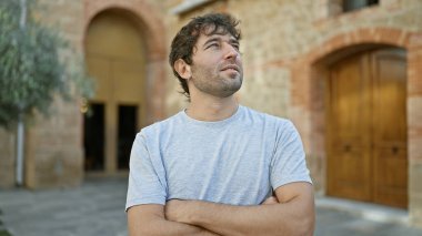 Sarışın sakallı neşeli genç adam, kollarını kavuşturarak gülümsüyor, yeşil ağaçlara bakarak yeşil şehir parkında gelişigüzel dikilirken mutluluğun tadını çıkarıyor..