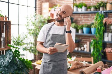 Genç, kel bir çiçekçi çiçekçide akıllı telefondan not defteri okuyor.