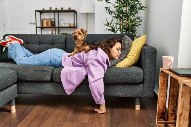 Genç, güzel, İspanyol bir kadın kanepede uzanıyor ve evde köpekle yatıyor.