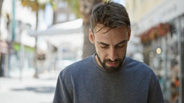 Yakışıklı bir İspanyol genç adam, sakin ama ciddi bir yüz ifadesi ile, şehir caddesinde aşağı bakan serin, güneşli gün ışığında dışarıda duran bir adam