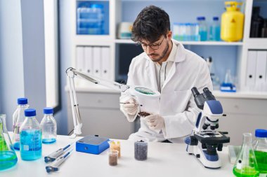 Young hispanic man scientist looking sample with loupe at laboratory