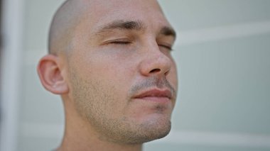 Genç İspanyol adam ciddi bir ifadeyle ayakta duruyor ve gözleri sokakta kapalı.