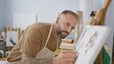 Yakışıklı genç adam, sanatsal ruhu serbest bırakılmış, rahat bir stüdyoda spatulayla resim çiziyor - rahat, ciddi bir sanatçının yolculuğu.