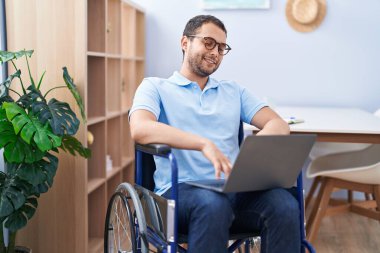 Young man using laptop sitting on wheelchair at home