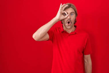 Kırmızı arka planda duran beyaz bıyıklı adam şaşırmış yüz ifadesiyle şaşırmış, parmaklarından bakan bir jest yapıyor. İnançsız ifade. 