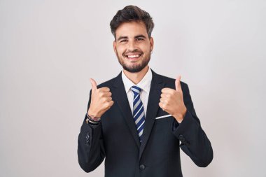 Dövmeleri olan, iş elbisesi giyen, kravat takan, el hareketleriyle olumlu jest yapan, gülümseyen ve mutlu genç bir İspanyol. Neşeli ifade ve kazanan jest. 