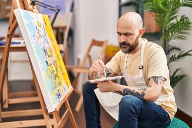 Sanat stüdyosunda ciddi bir ifadeyle çizim yapan genç kel adam.