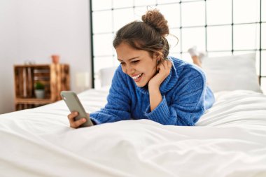 Yatakta uzanmış akıllı telefon kullanan genç, güzel İspanyol kadın.