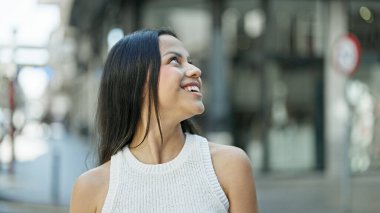 Young beautiful hispanic woman smiling confident looking to the sky at street