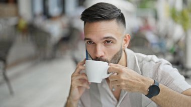 Genç İspanyol adam akıllı telefonda konuşuyor. Kahve dükkanının terasında kahve içiyor.