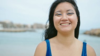 Genç Çinli turist kumsalda kendine güvenen bikini giyiyor.