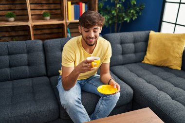 Genç Arap adam evdeki kanepede kahve içiyor.