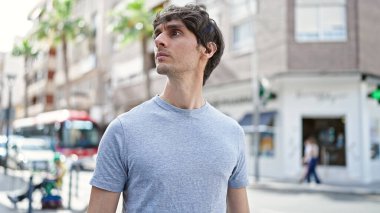 Latin kökenli genç adam ciddi bir ifadeyle sokağa bakıyor.