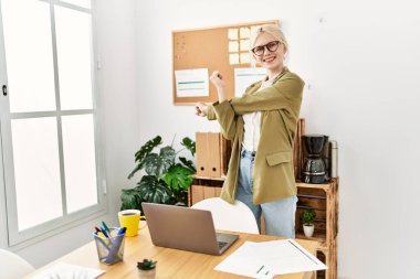 Genç sarışın iş kadını ofiste kollarını açmış duruyor.