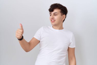 Gündelik beyaz tişört giyen, gururlu, gülümseyen, baş parmak kaldıran genç, ikili olmayan bir adam. 