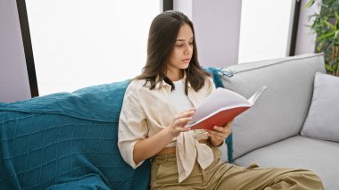 Evdeki kanepede oturmuş kitap okuyan güzel İspanyol kadın.