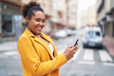 Afro-Amerikalı kadın sokakta akıllı telefon kullanarak kendine güveniyor.